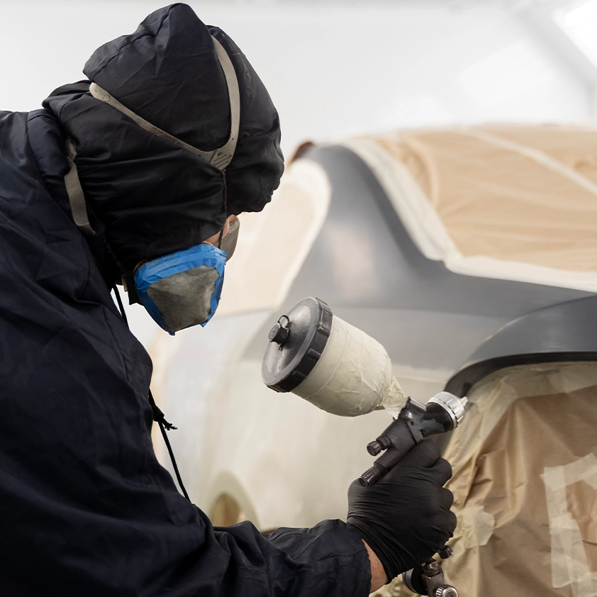 Technician spray painting a car panel in a paint booth